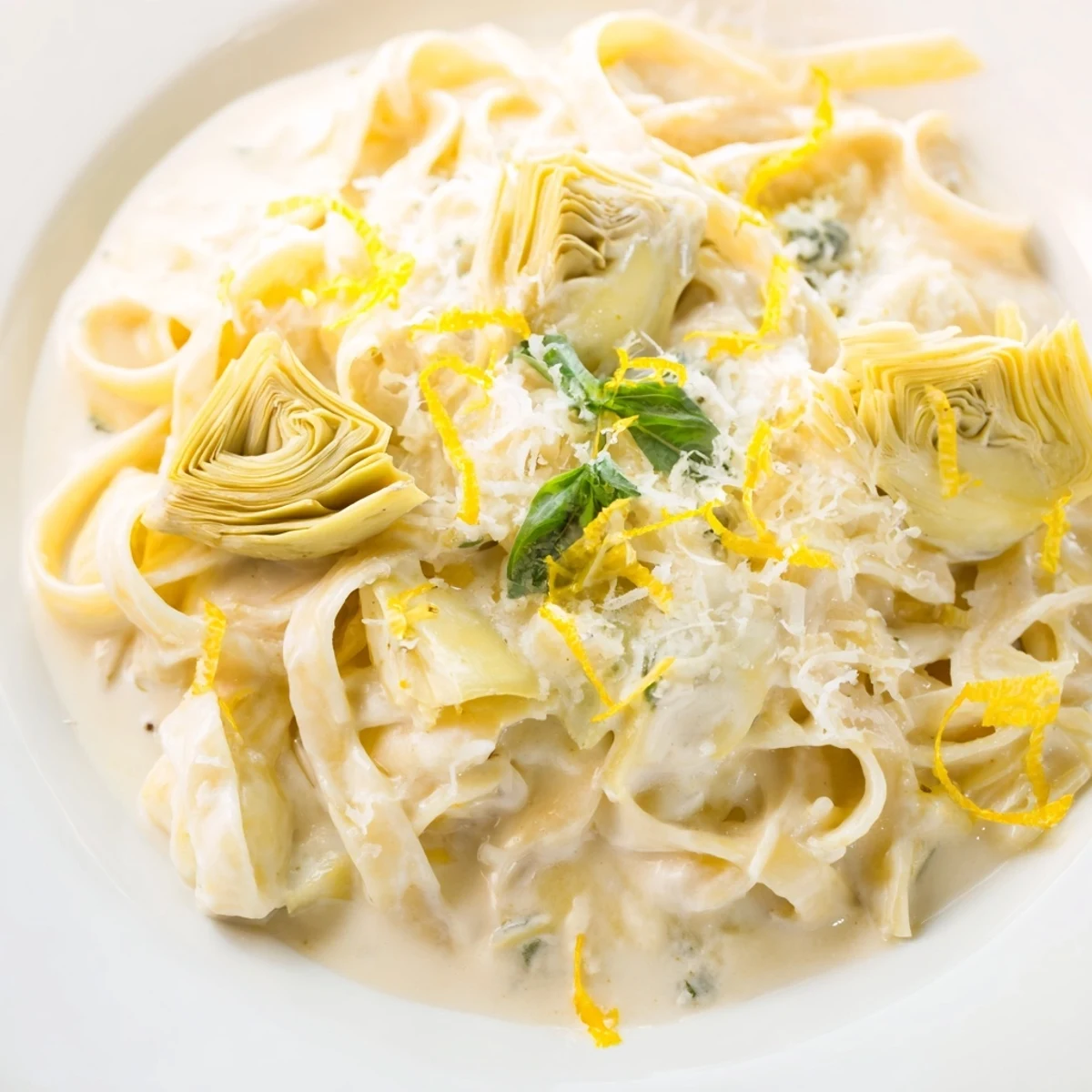 A steaming bowl of Creamy Lemon Artichoke Pasta: Cheesy, lemony pasta with bright green spinach and artichokes.
