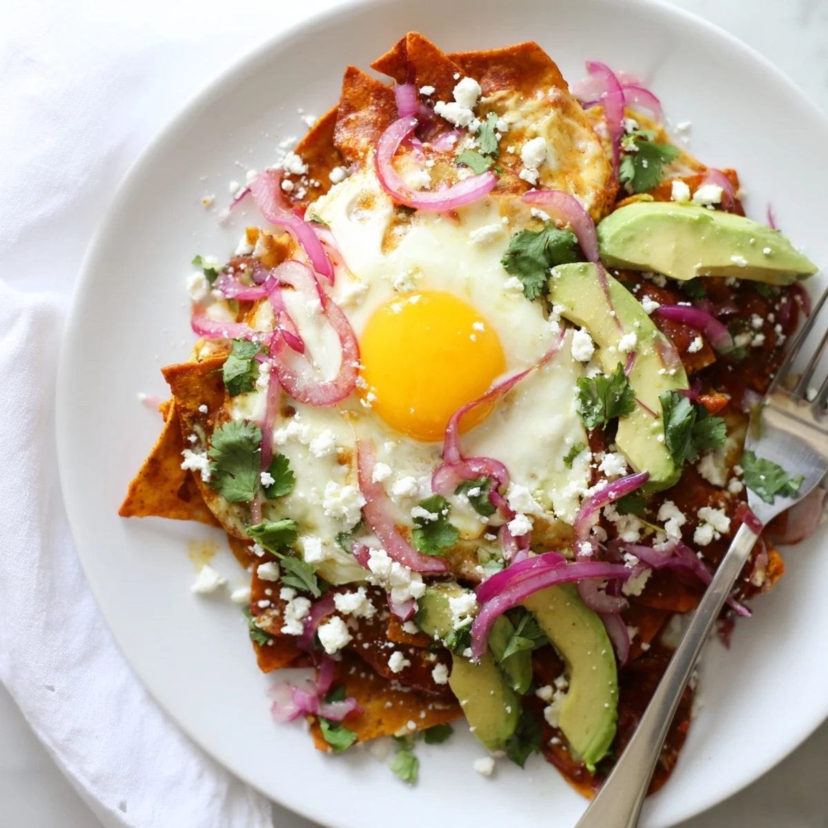Golden tortilla chips simmered in spicy salsa roja, crowned with a runny-yolk egg and garnished with jalapeños and radishes for a flavorful kick.