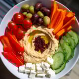 Hearty Middle Eastern Mezze Platter features a generous bowl of hummus topped with olive oil and sumac, surrounded by colorful salads and cheese.