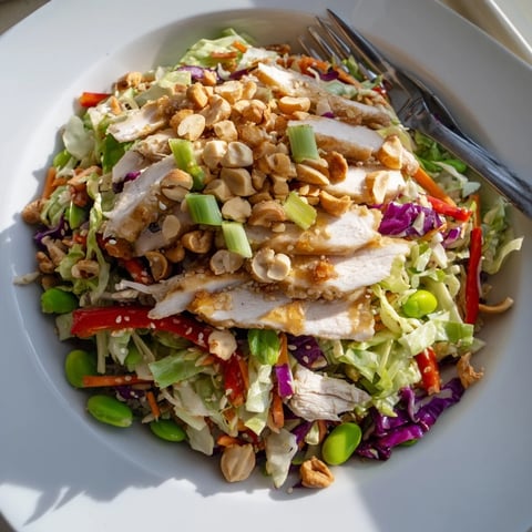 A close-up of the Edamame Crunch Chicken Salad shows colorful shreds of green and red cabbage, carrots, and tender chicken tossed in a glossy ginger dressing.