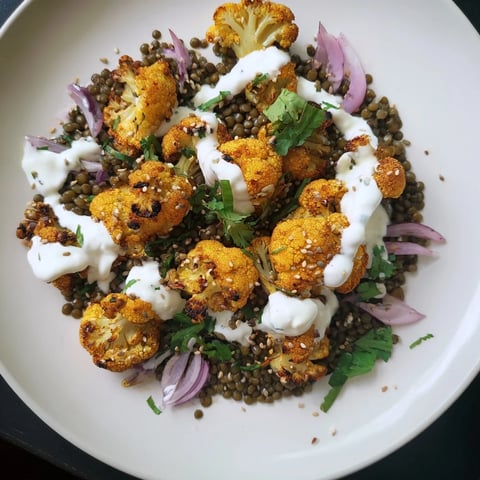 Golden roasted cauliflower florets seasoned with cumin and paprika sit atop a vibrant bed of lemon lentils, ready for a creamy drizzle of tahini yogurt sauce.