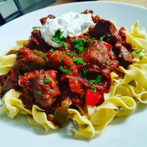 Fork-tender beef in savory stew, served over buttered noodles, showcasing the delicious Hungarian Goulash.