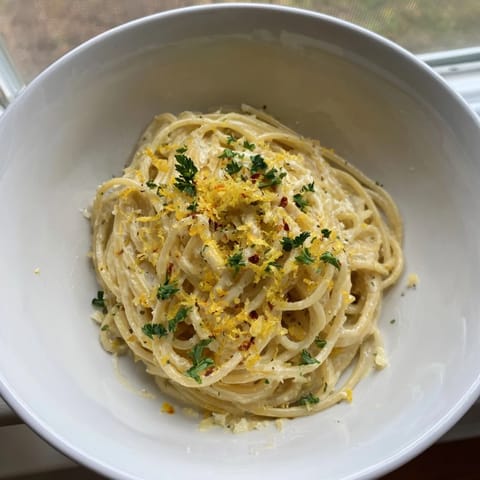 A bowl of fresh Lemon-Garlic Greek Yogurt Pasta topped with grated Parmesan and lemon zest.