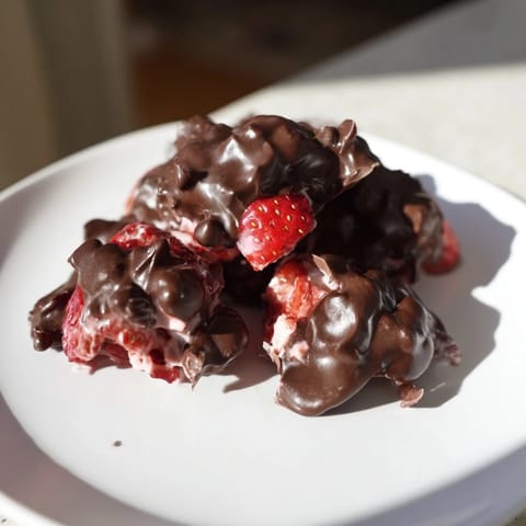 Vibrant red strawberries peek through the melted chocolate surrounding these homemade Strawberry Yogurt Clusters.