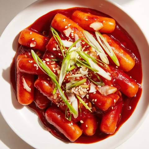 Chewy rice cakes in vibrant Korean tteokbokki simmer beside soft boiled eggs and onion slices.