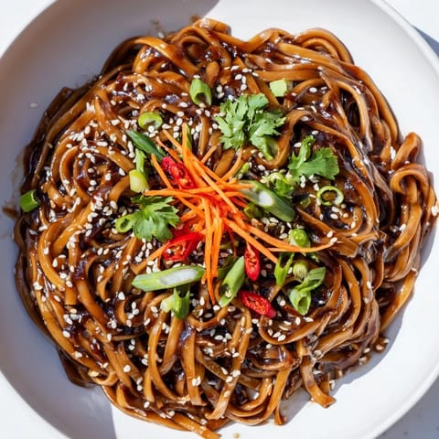 Close-up of steaming Asian Garlic Noodle Bowl in a ceramic dish, showcasing al dente noodles coated in savory garlic, soy, and sesame oil.