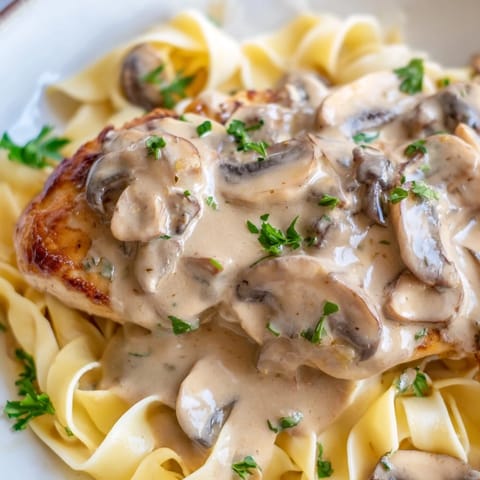 A close-up of tender chicken Marsala with rich wine sauce and sautéed cremini mushrooms, garnished with fresh parsley.  