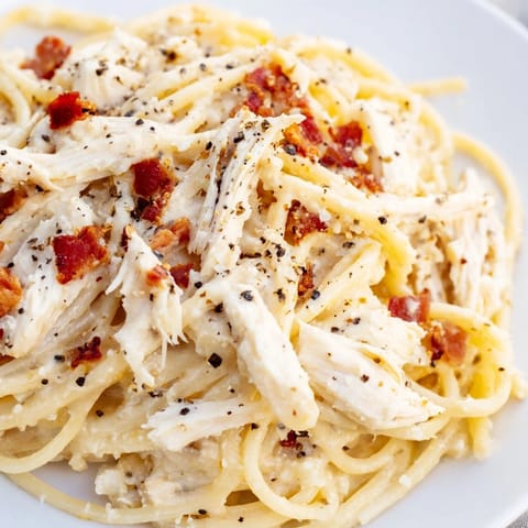 Served in a white bowl, the Chicken Carbonara is garnished with fresh parsley and extra Parmesan.