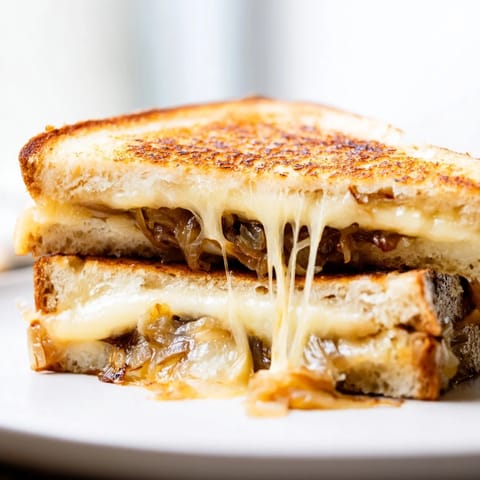 Golden-brown grilled cheese sandwiches feature nutty Gruyère and slow-cooked caramelized onions, stacked beside a fresh green salad.
