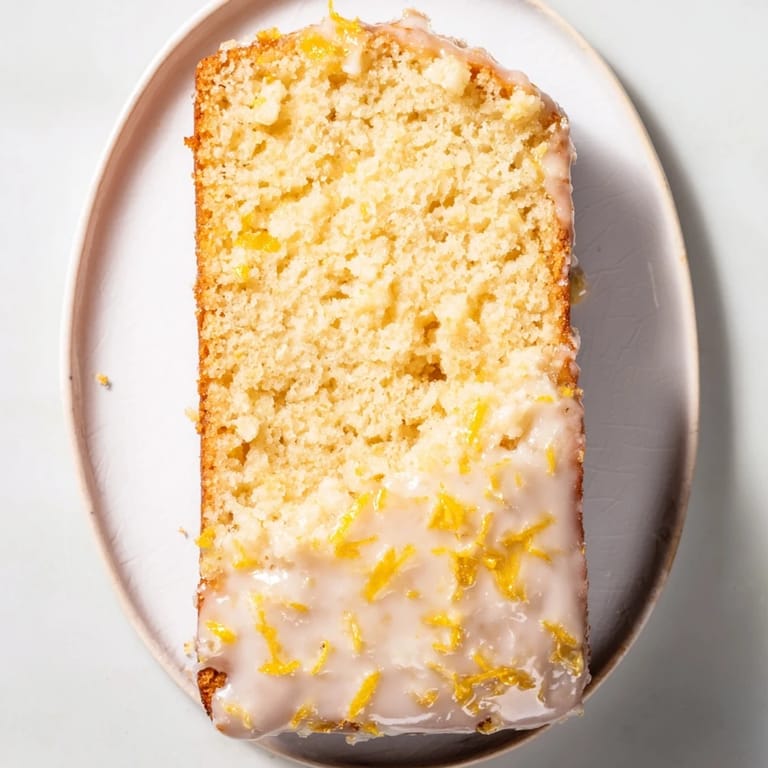 A close-up of a golden brown lemon loaf cake topped with sweet, drizzled lemon icing.