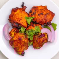 Golden-brown Indian Tikka Spiced Chicken pieces roasted to perfection on a wire rack, garnished with fresh cilantro and lemon wedges for serving.  