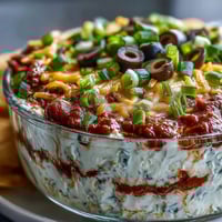 Four layered dip with refried beans, sour cream, salsa, and cheddar cheese topped with olives and green onions.